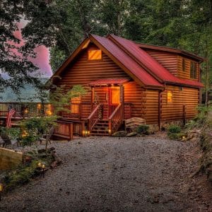 cabin on hill with lights on and gravel drive