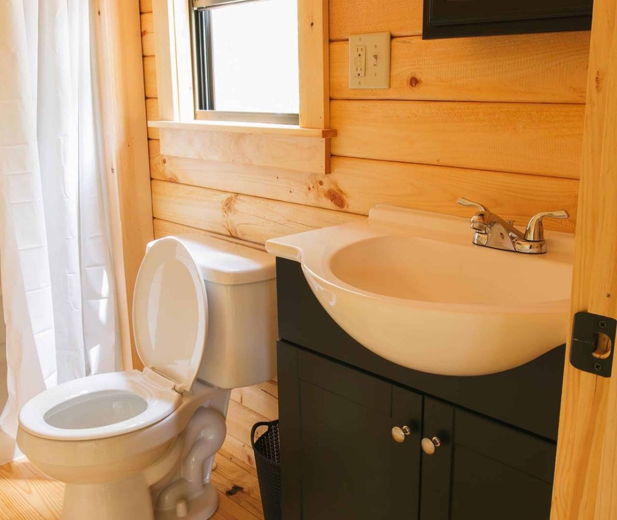 dark cabinet below white bowl sink in bathroom next to toilet under window